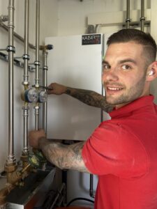 Ein Installateur überprüft Heizungsrohre in einem technischen Raum mit einem Werkzeug.