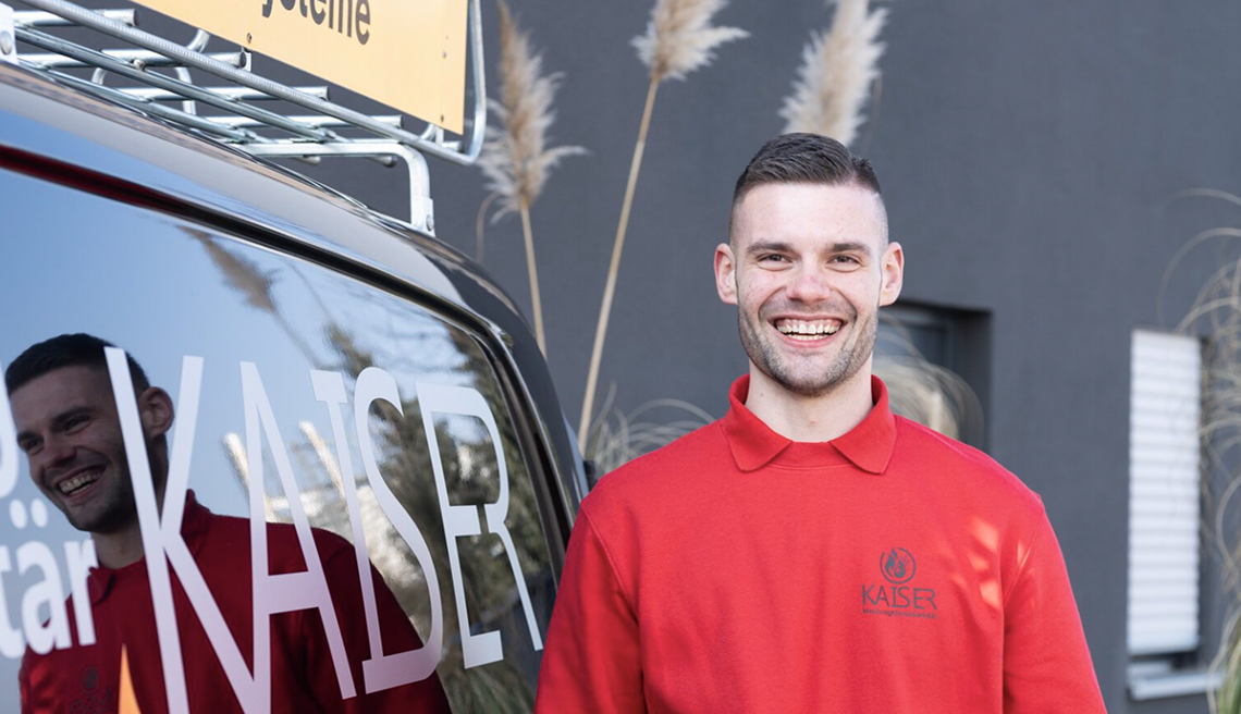 Lächelnder Mitarbeiter von Kaiser Heizungs- und Sanitärtechnik steht neben einem Fahrzeug mit dem Firmenlogo.