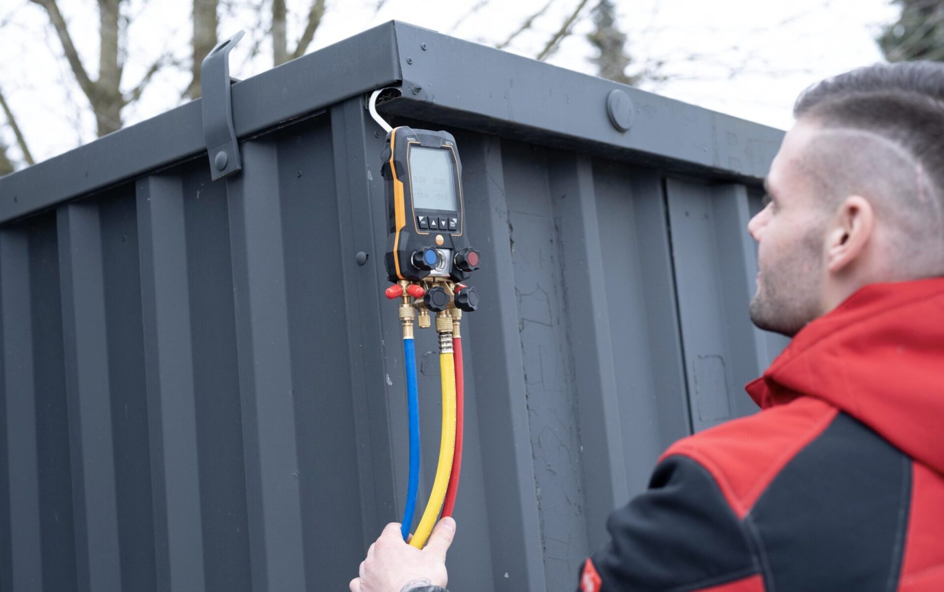 Techniker verwendet ein digitales Messgerät mit farbigen Schläuchen an einem Container.